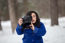 a woman in a coat taking a picture of snow 