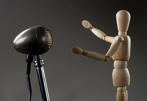 Wooden dummy singer singing into antique microphone .