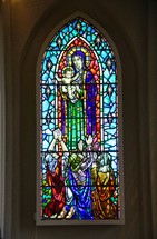 Stained glass window depicting Mary, Baby Jesus, and worshippers.