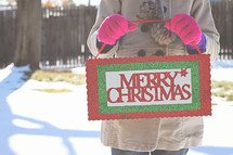 a woman holding a Merry Christmas sign 