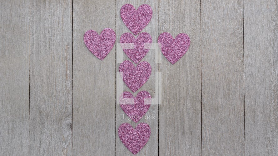 a cross of pink hearts on gray wood background 