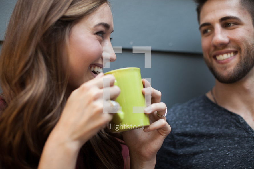 A young man and woman smiling at each other and drinking coffee.
