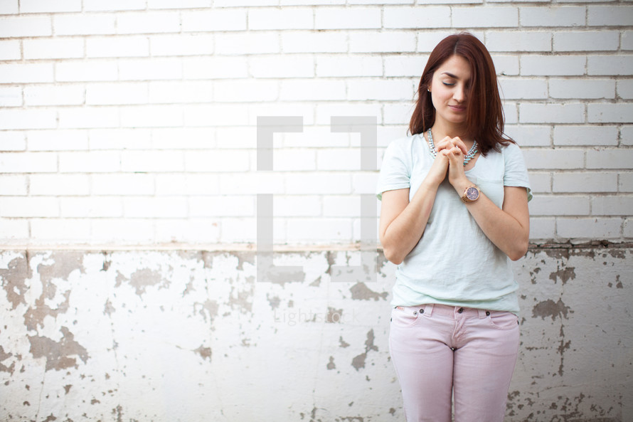a young woman with praying hands standing in front of a white wall 