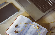 earbuds on the pages of a Bible and a laptop computer 