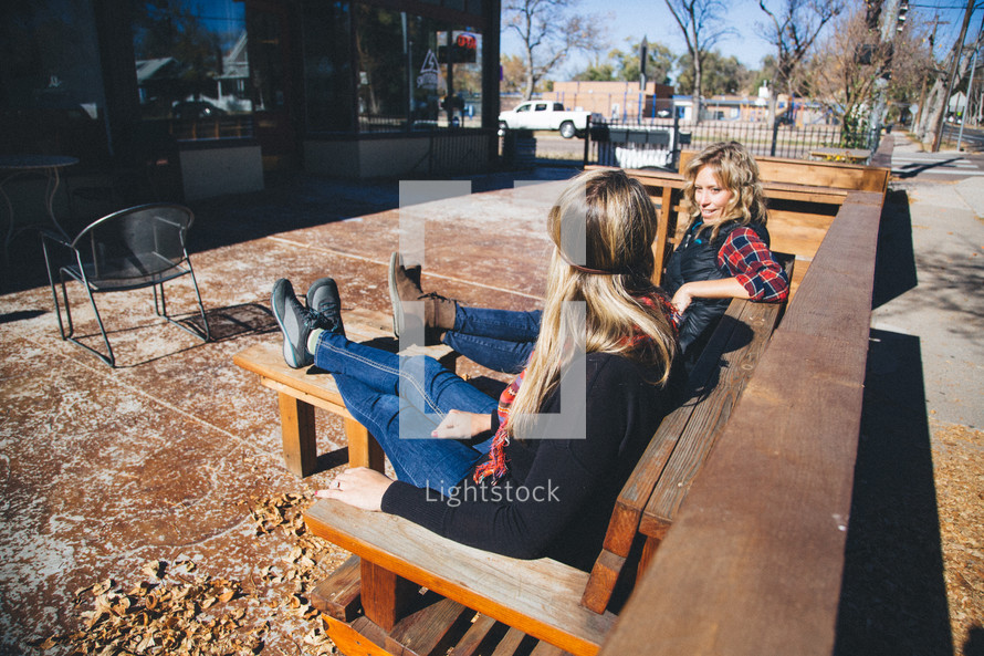 women sitting outdoors on a bench in front of a restaurant talking 