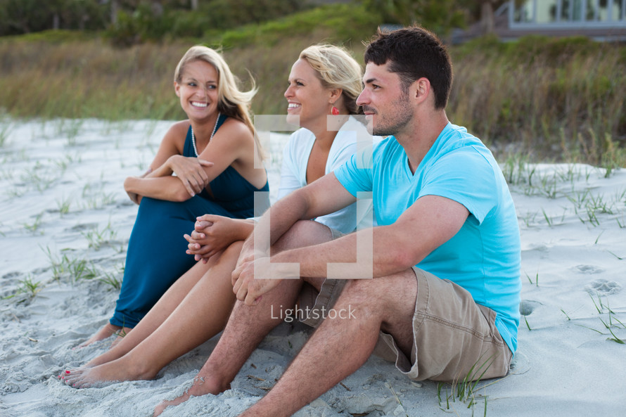 friends sitting in the sand talking on a beach 
