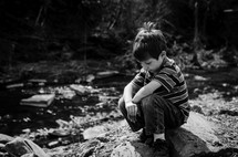 a boy child squatting on a rock 