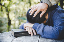 Asian woman with her Bible while being prayed for with a hand on her head