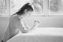a woman kneeling in prayer by her bedside