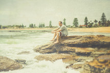 A man sitting on rocks at an ocean shore