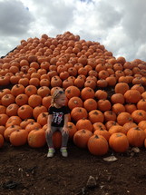 a girl child sitting on a pile of pumpkins 