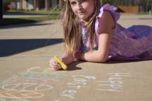 A little girl coloring Happy Easter and eggs with sidewalk chalk 