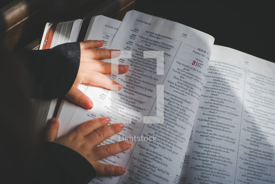 a child's hands on the pages of a Bible 