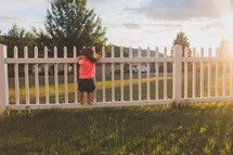 toddler girl standing on a white picket fence 