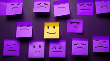 Upset faces with one smiling face drawn on sticky notes. 