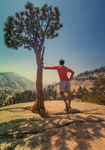 man leaning against a pine tree taking in the views 