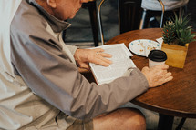 elderly man sitting at a table reading a Bible 
