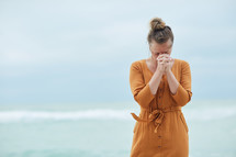 a woman standing on a beach praying 