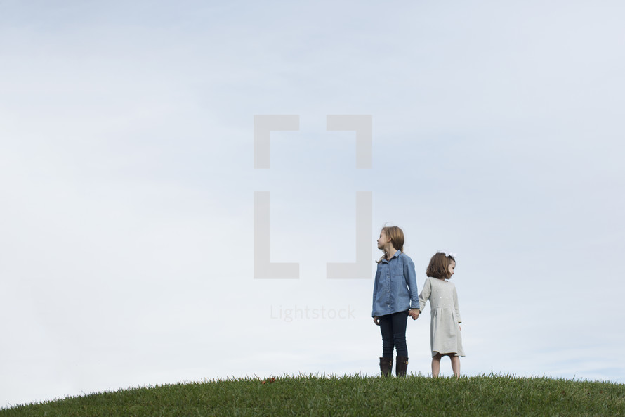 sisters standing on a hilltop holding hands 
