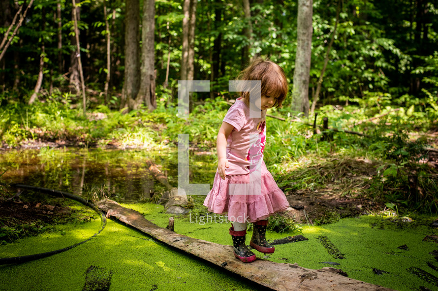 a toddler girl in rain boots exploring a pond 