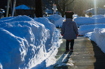 toddler girl on a plowed sidewalk in the snow 
