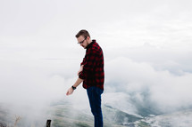 man in a plaid shirt standing on a mountaintop 