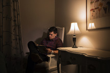 A man sitting and reading a book near a lamp.