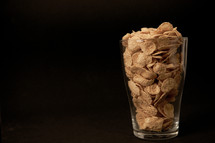 cornflakes with milk in a transparent glass against a black background with place for text
