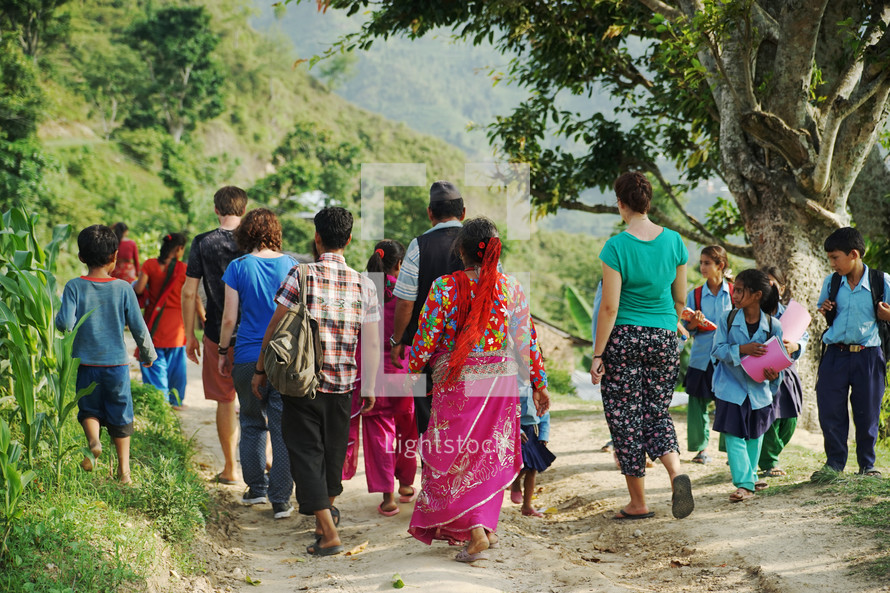 school children and villagers walking on a dirt path 