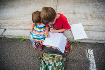 a boy drawing in a notebook and sister watching 