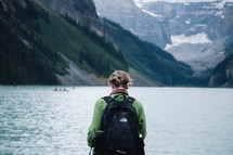 a woman with a backpack standing in front of a lake 
