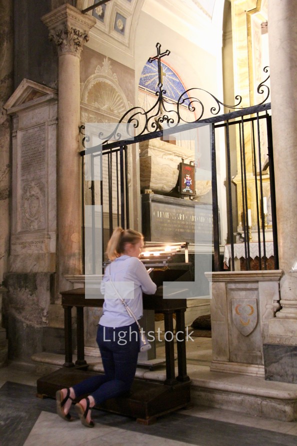 a woman praying at a kneeling bench in a cathedral 