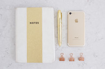 A notebook, gold pen, cell phone and paper clips.