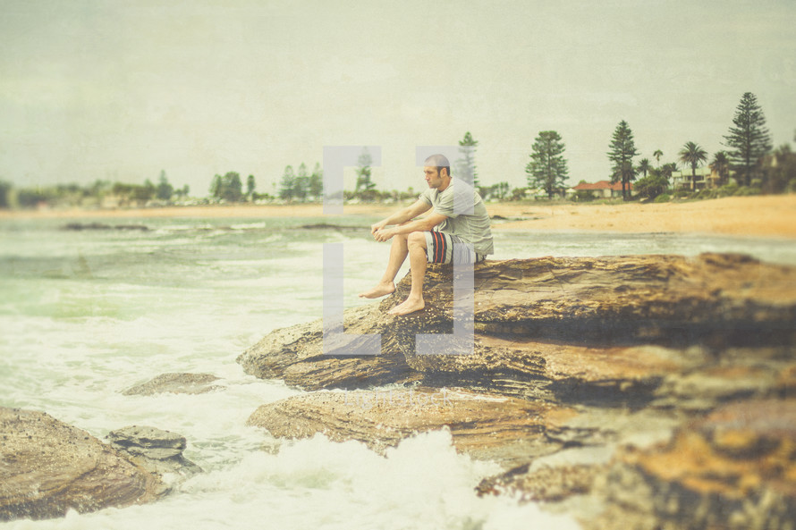 A man sitting on rocks at an ocean shore