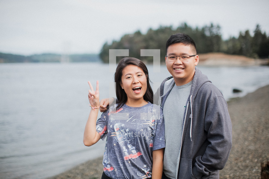 a couple standing by a river shore giving peace signs 