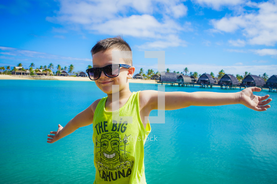 a boy in sunglasses standing in front of cabins on stilts 