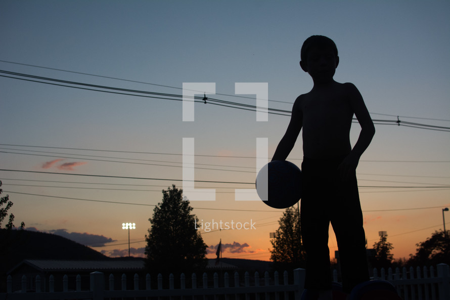 silhouette of a boy child holding a basketball at sunset 