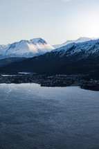 snow on mountains and homes along a shore 