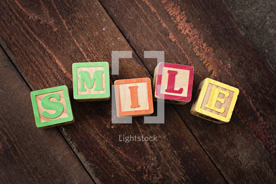 "SMILE" spelled out with colorful wooden children's blocks on a wooden surface.