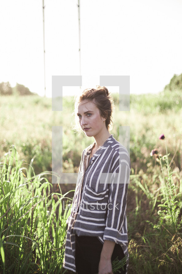 woman in a field of tall grass wearing a flowing shirt 