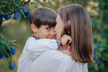 Tender scene of loving son with mom on plum orchard backdrop with sunlight. Beautiful family. Cute 4 years old kid with mother. Parenthood, childhood, happiness, children wellbeing concept.