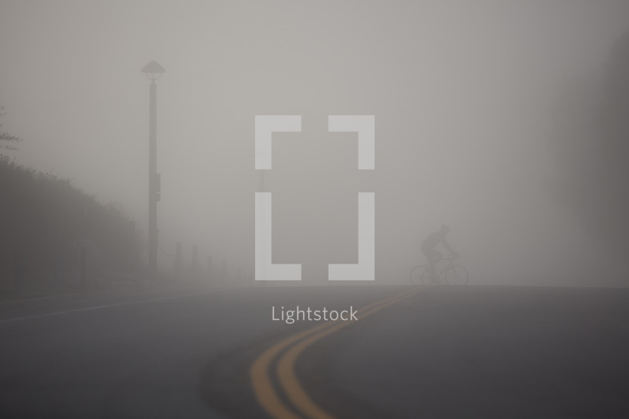 man riding a bicycle across a street under thick fog