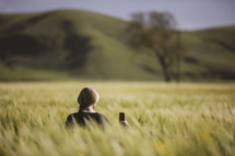 a woman holding a cellphone standing in a field of tall grasses 