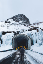 man standing in front of a mountain road tunnel in winter 