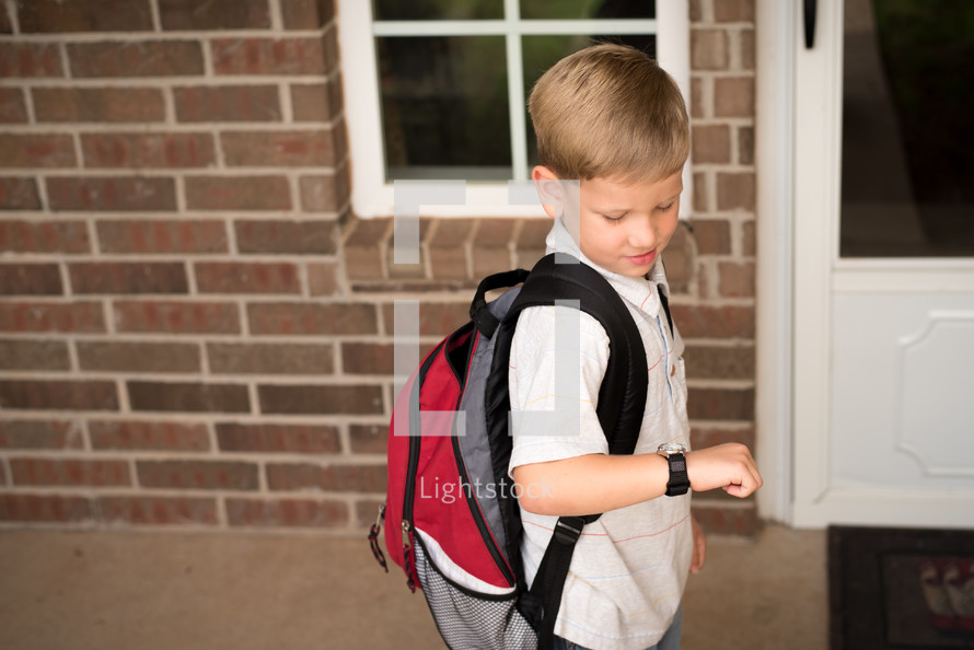 a little boy with a book bag looking at his watch 