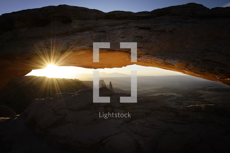 sunburst through a rock arch overlooking a canyon 