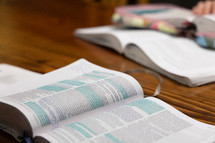 Open Bibles laying on table with blue highlighter on pieces of text, closer view of text, Bible on top of study book
