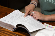 Woman reading Bible during Bible study time in a discipleship group, hands on pages, looking for page number of a book, pointing, holding highlighter
