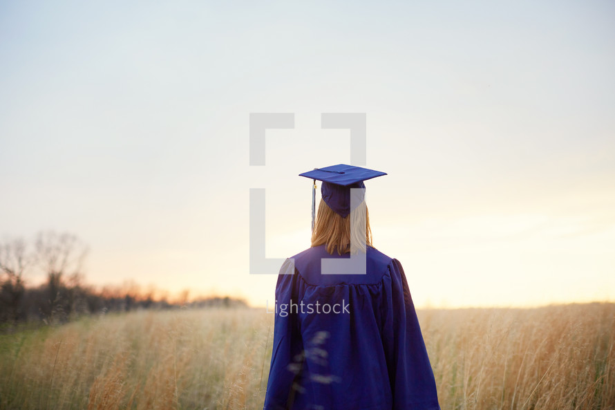 female graduate walking through a field 