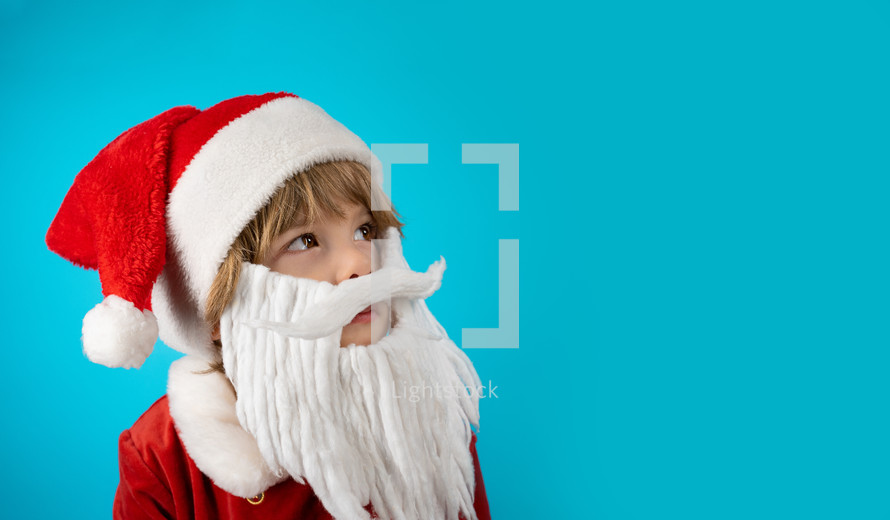 Portrait of adorable boy in Santa Claus hat on blue studio background. Christmas celebration. Happy childhood, kid, lovely son. Copy space. High quality photo